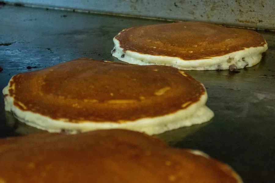 Three pancakes cooking on the diner's flat top griddle